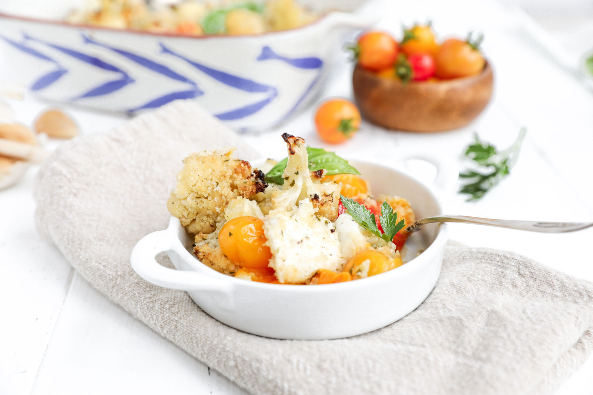 An individual bowl of cauliflower casserole with a bowl of tomatoes behind it. 