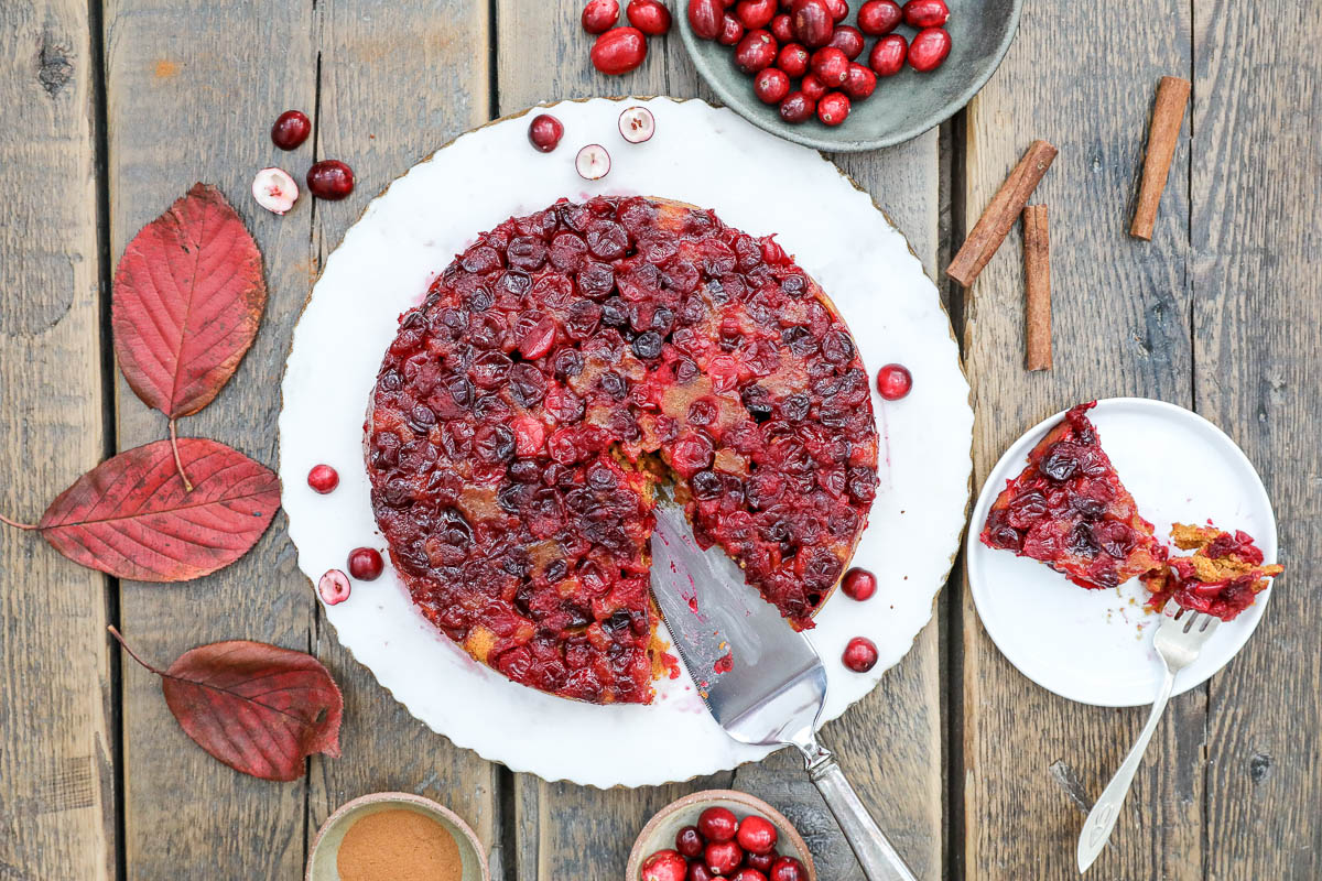 An overhead image of a cranberry upside down cake on a white plate with a silver cake cutter.