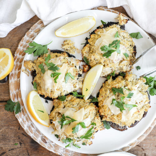 An overhead image of stuffed portabello mushrooms on a white plate with lemon wedges and a tongs.