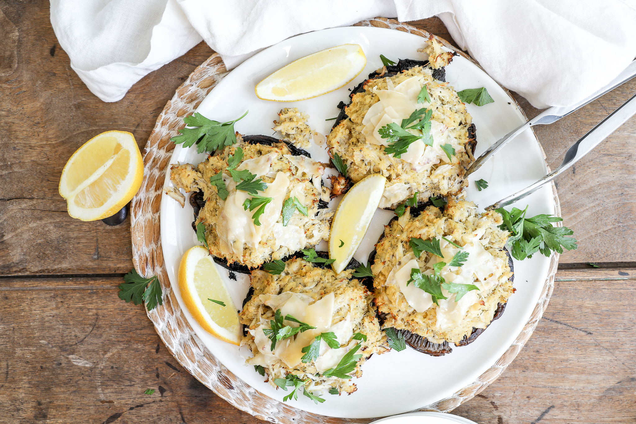 An overhead image of stuffed portabello mushrooms on a white plate with lemon wedges and a tongs.