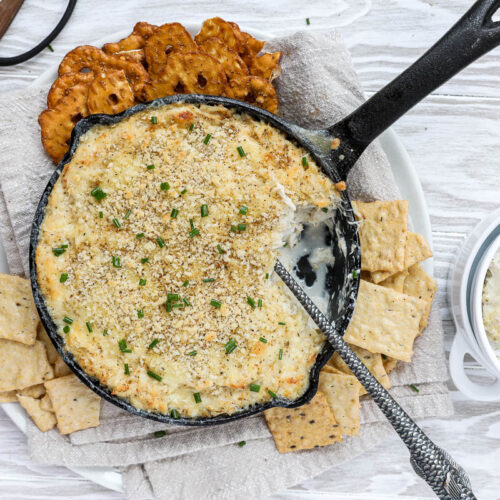 An overhead image of a warm crab dip with crackers and pretzels.
