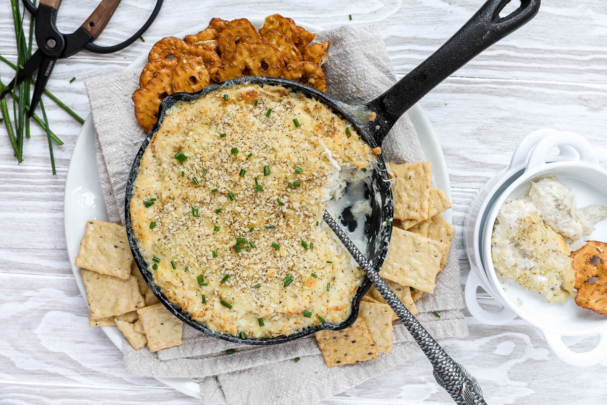 An overhead image of a warm crab dip with crackers and pretzels.