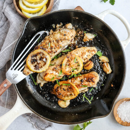 An overhead image of pan fried monkfish in a skillet with lemon slices on a white countertop.