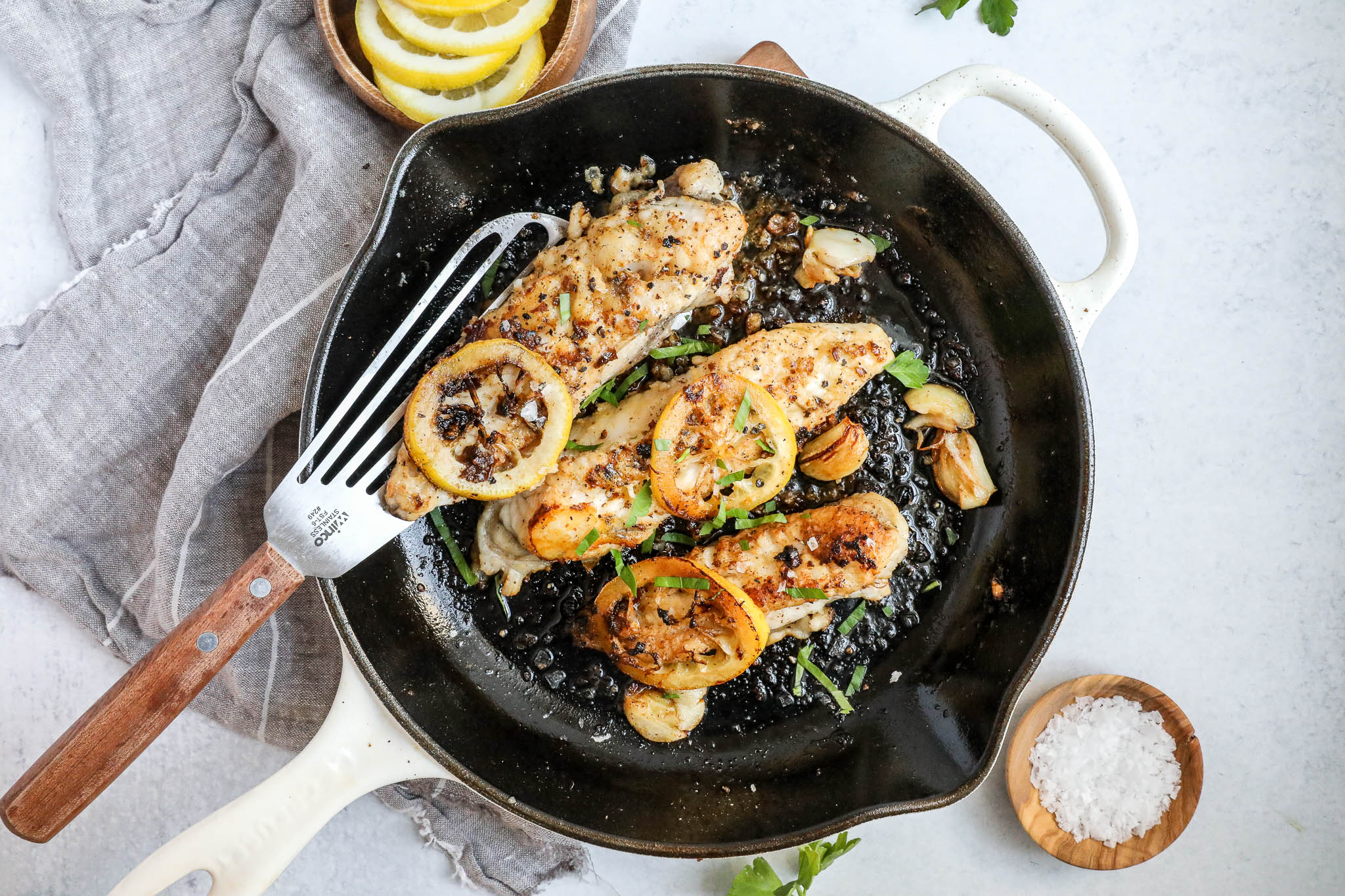 An overhead image of pan fried monkfish in a skillet with lemon slices on a white countertop.