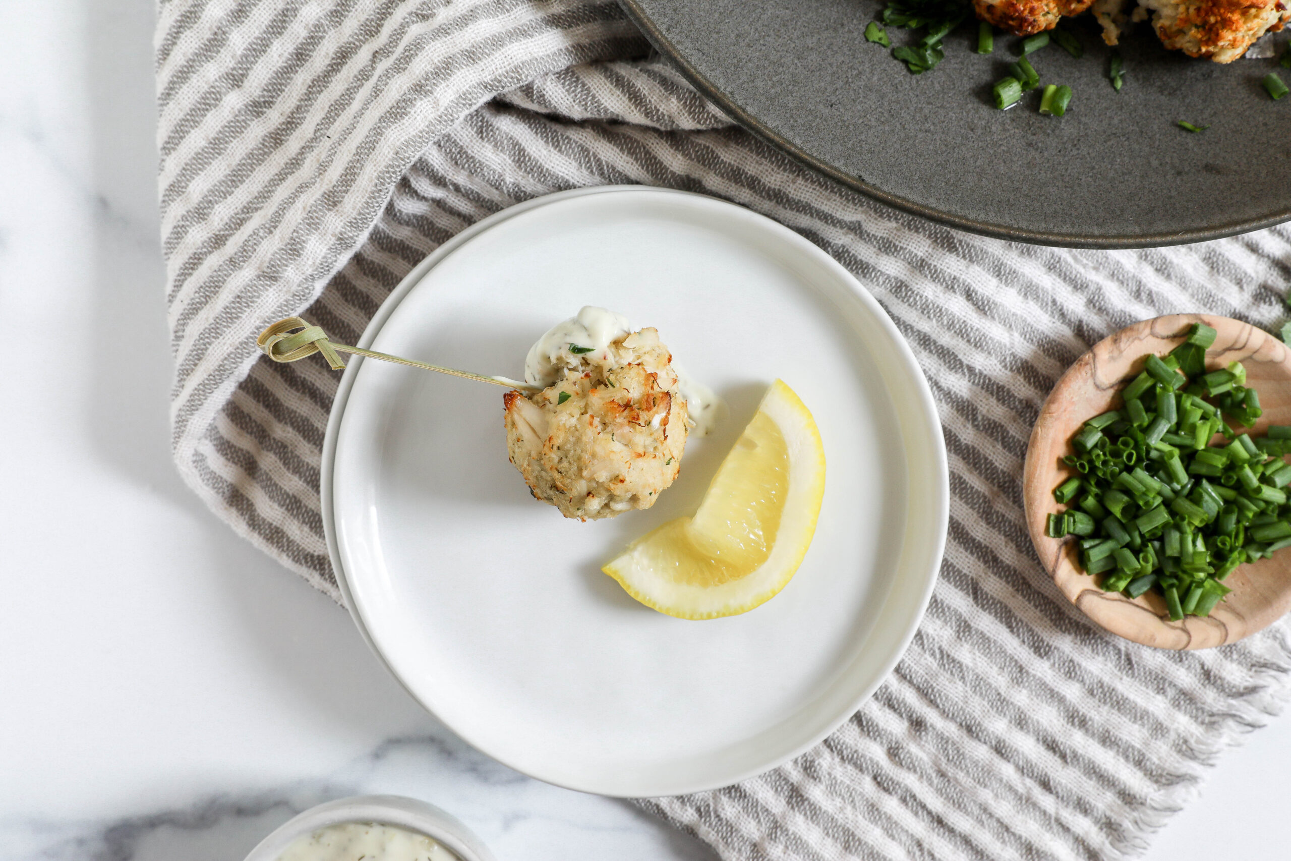An overhead image of an air fryer crab cake dipped in tartar sauce with a toothpick on a white plate.