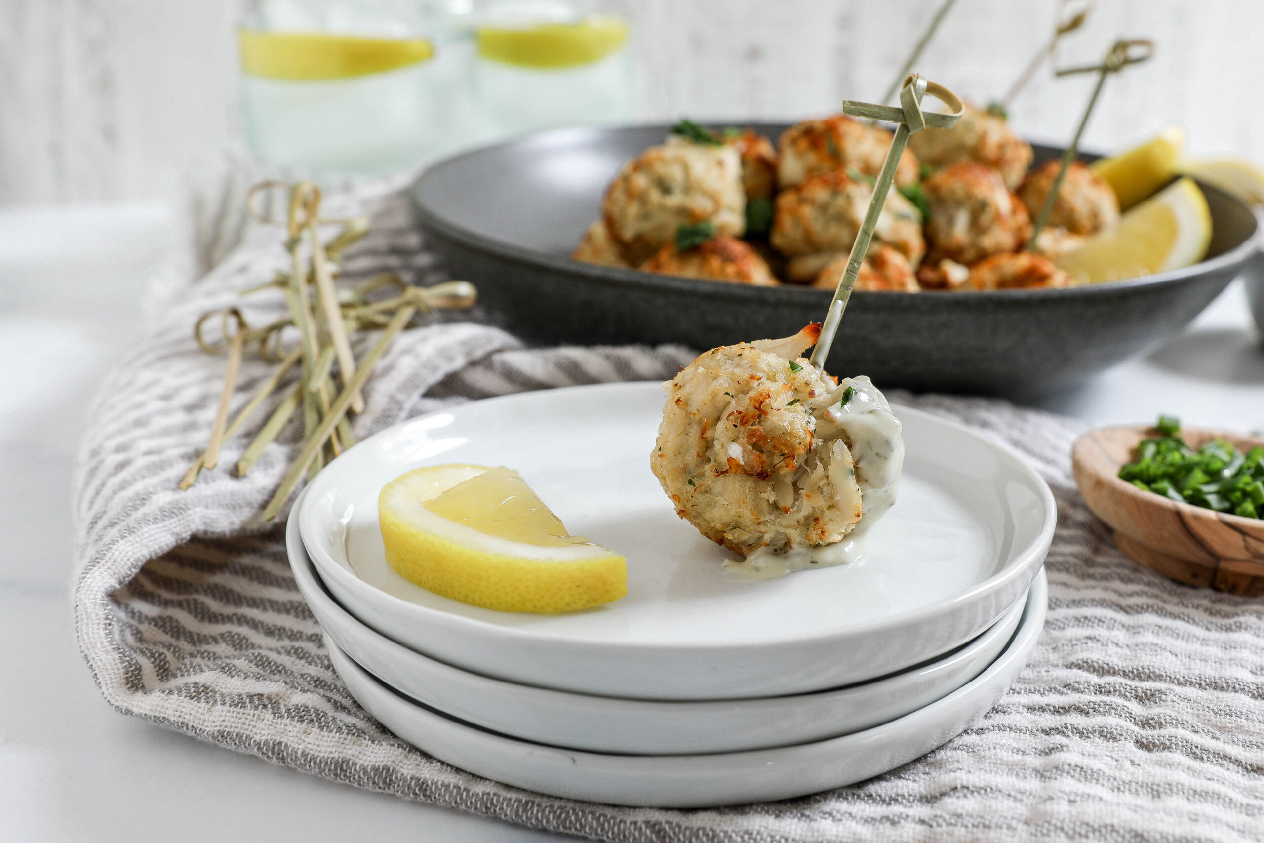 An image of an air fryer crab cake dipped in tartar sauce with a toothpick on a stack of white plates.