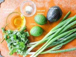 An overhead image of ingredients needed to make an avocado crema - avocado, cilantro, scallions, salt and pepper and olive oil.