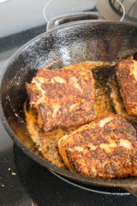 An image of cod being blackened in a cast-iron skillet.
