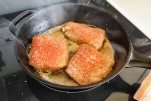 An image of blackened cod just being added to the skillet.
