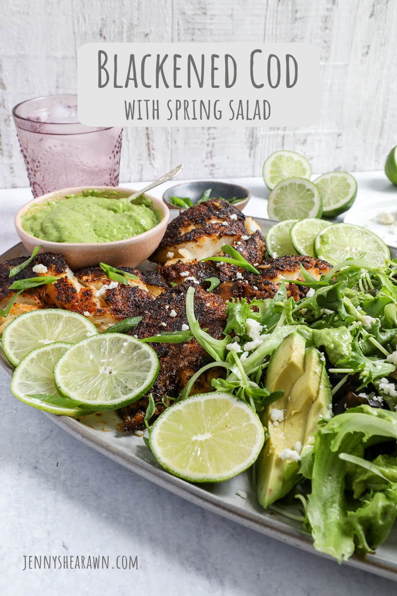 An image of a blackened cod recipe with a spring salad, avocado sauce and lime wedges.