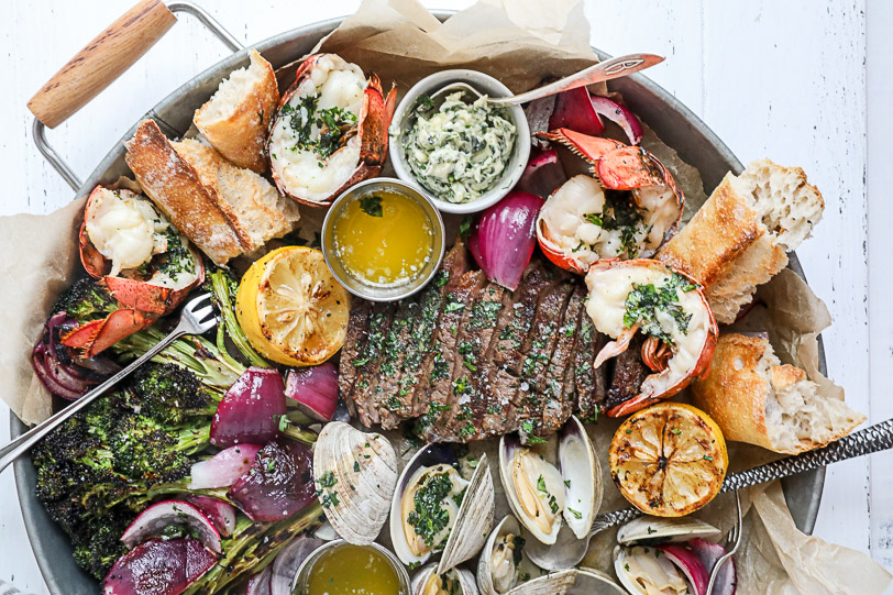 A silver platter with steak, lobster and clams. 