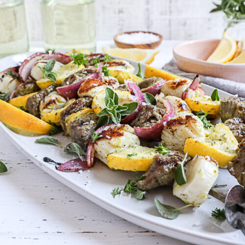 An image of steak and scallop kabobs on a white plate.