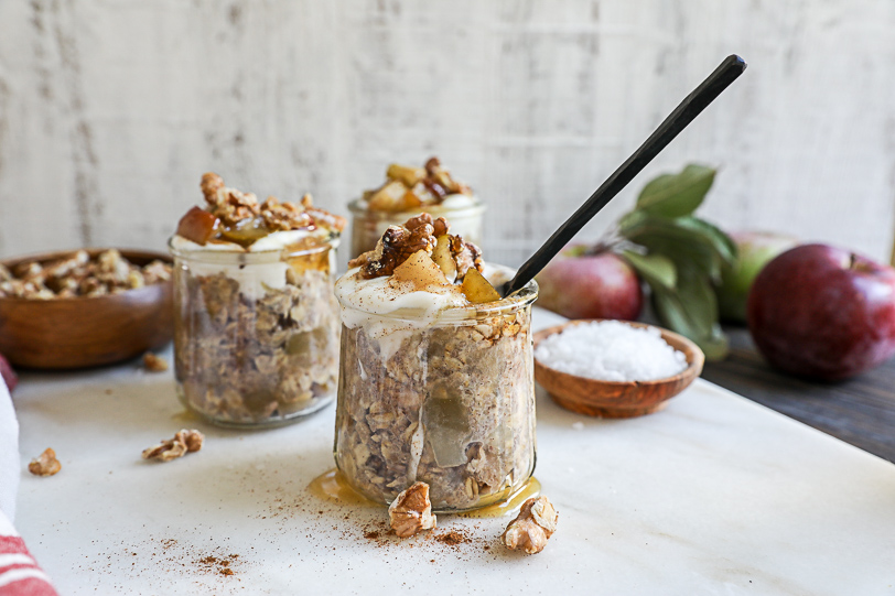 An image of a few clear jars of overnight oats topped with yogurt and chopped apples and honey.