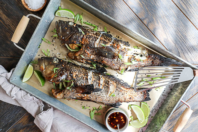 An image of 2 whole black sea bass on a platter with a fish spatual and a small bowl of soy sauce. 