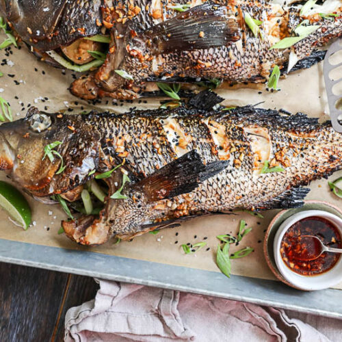 An image of a whole grilled black sea bass sprinkled with soy sauce and sliced scallions.