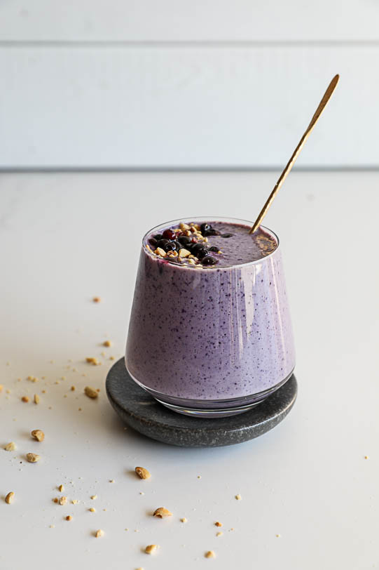 An image of a wild blueberry smoothie in a glass with peanuts scattered around