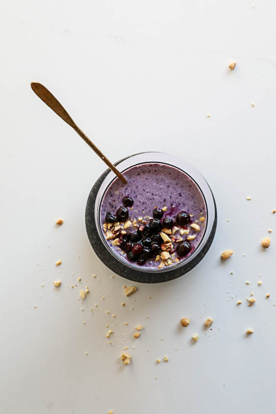 An overhead image of a peanut butter and jelly smoothie with crushed peanuts scattered around it