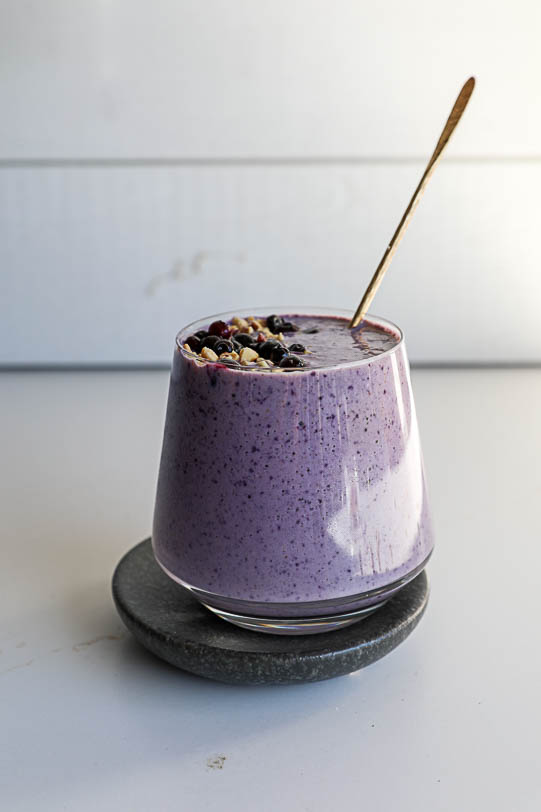 A pb&j wild blueberry smoothie with a gold straw on a white countertop. 