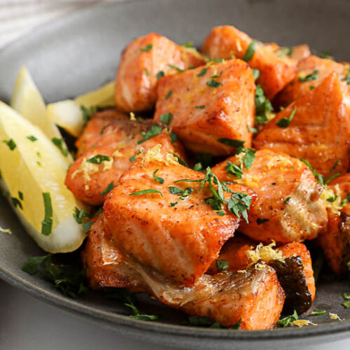 An image of air fryer salmon bites in a black bowl with lemon wedges on the side.