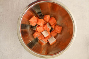 Raw salmon chunks in a large metal bowl.
