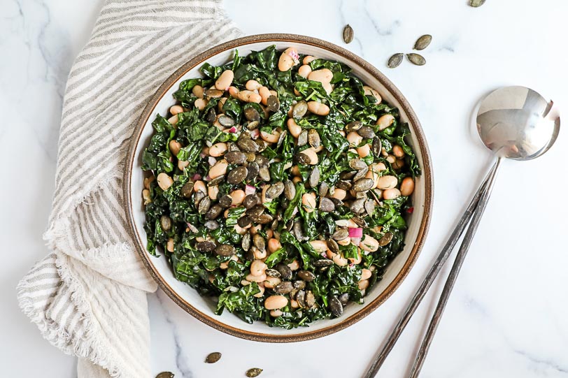 An overhead image of a kale and white bean salad with pumpkin seeds.