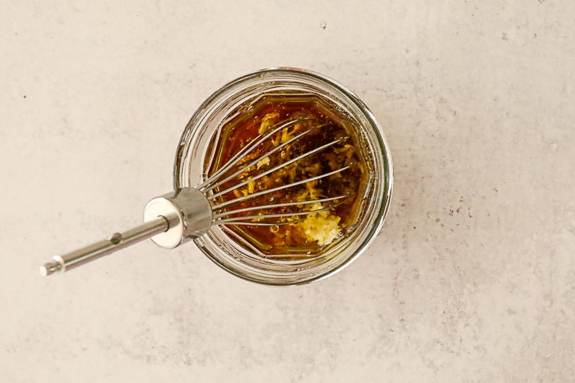 An overhead image of a vinaigrette in a small mason jar with a whisk. 