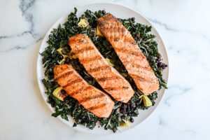An image of a grilled salmon salad with kale on a white plate.