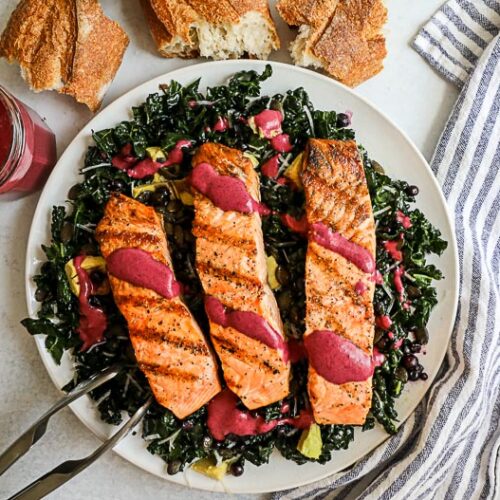 An overhead image of a salmon kale salad on a white plate with a striped napkin with chunks of crusty bread on the side.