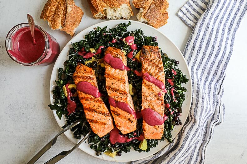 An overhead image of a salmon kale salad on a white plate with a striped napkin with chunks of crusty bread on the side.