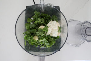 An image of ingredients for a cilantro sauce in a food processor. 
