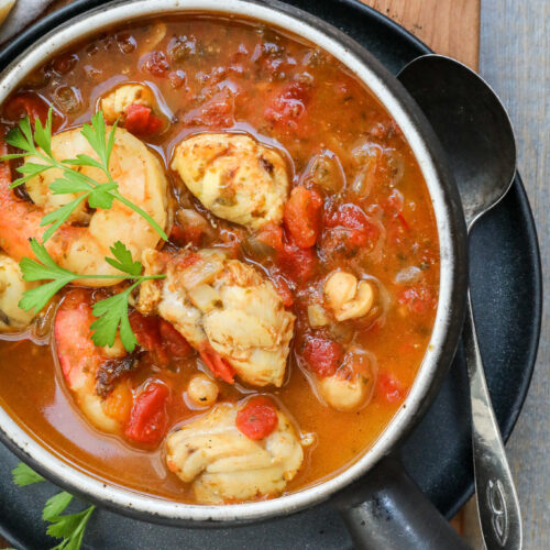 An overhead image of monkfish stew in a black bowl on a wooden counter.