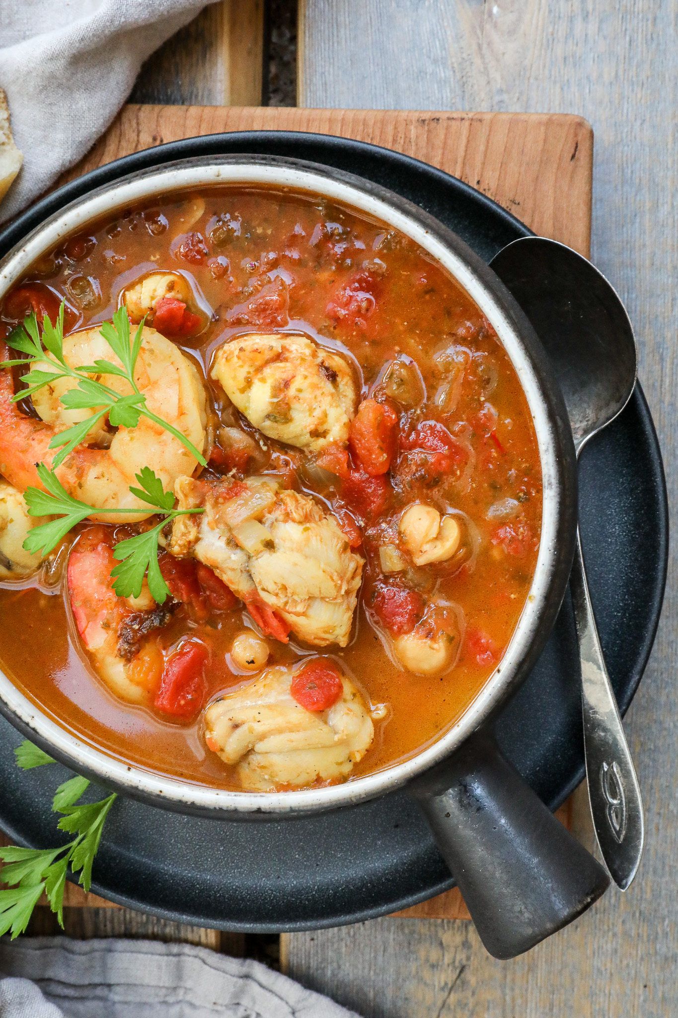 An overhead image of monkfish stew in a black bowl on a wooden counter.