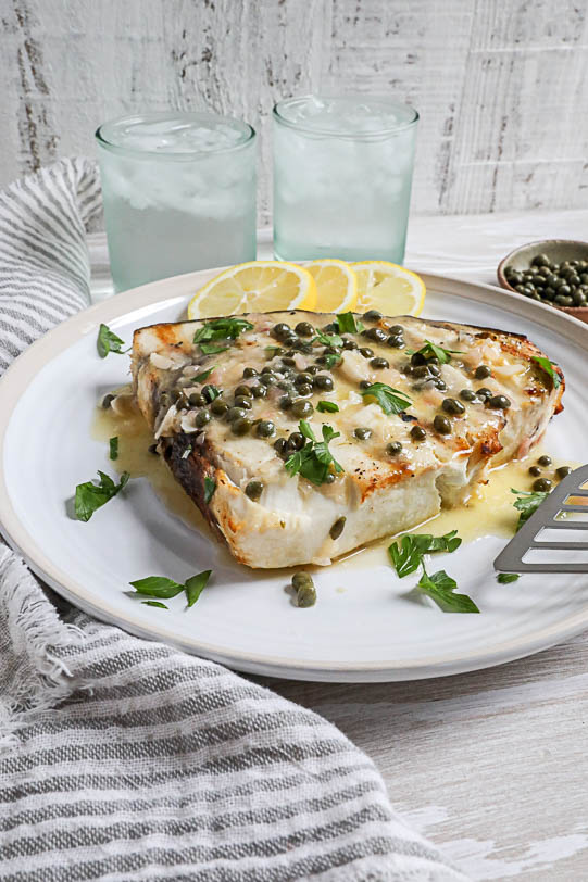 An image of a swordfish piccata recipe with lemon slices and water glasses.