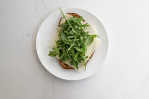 An image of whole wheat bread with cheddar and arugula.