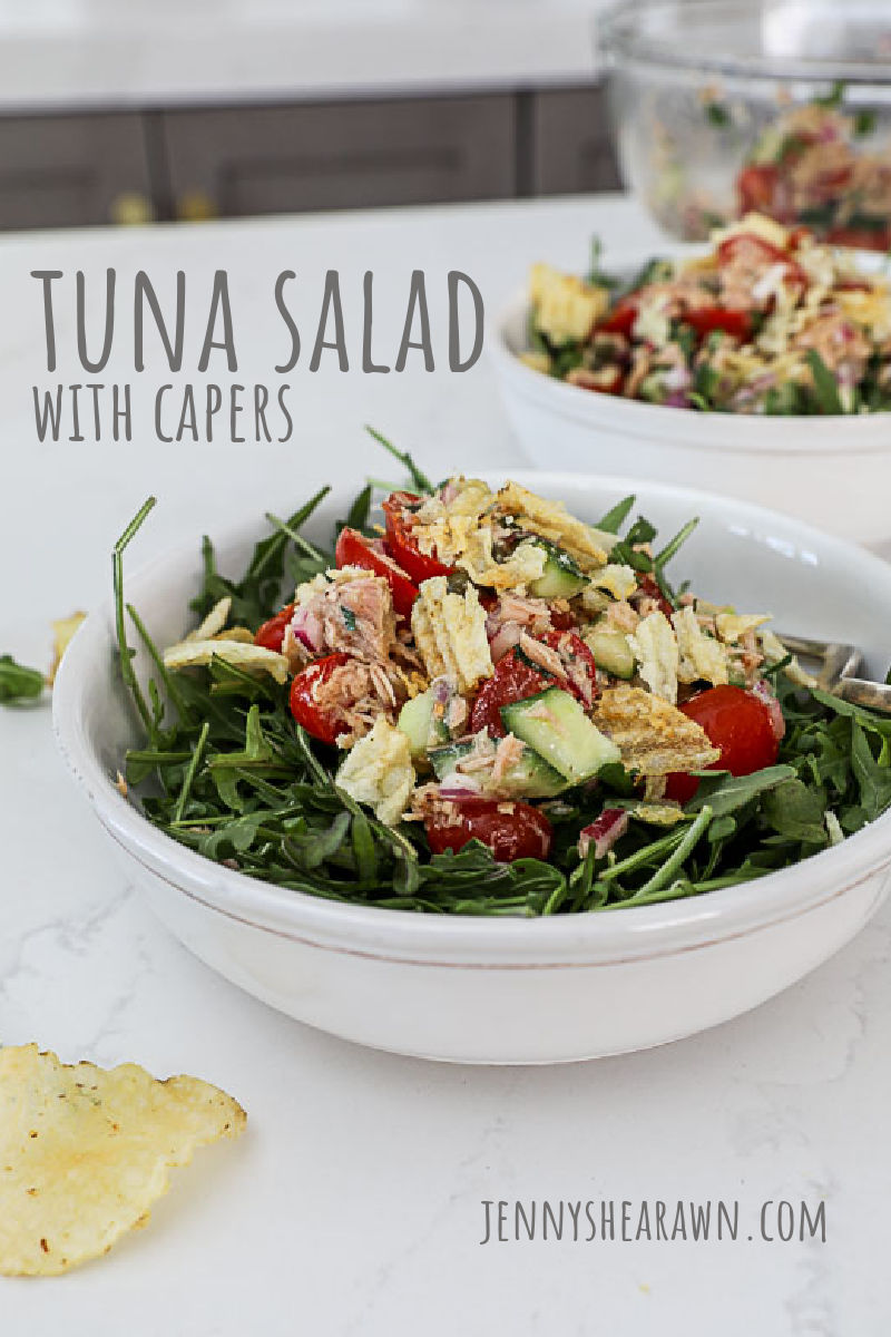 An image of tuna salad with capers over arugula in a white bowl.