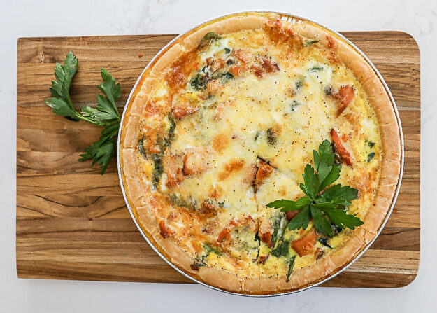 An overhead image of a whole quiche on a cutting board.