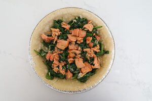 An overhead image of a pie crust with spinach and salmon.