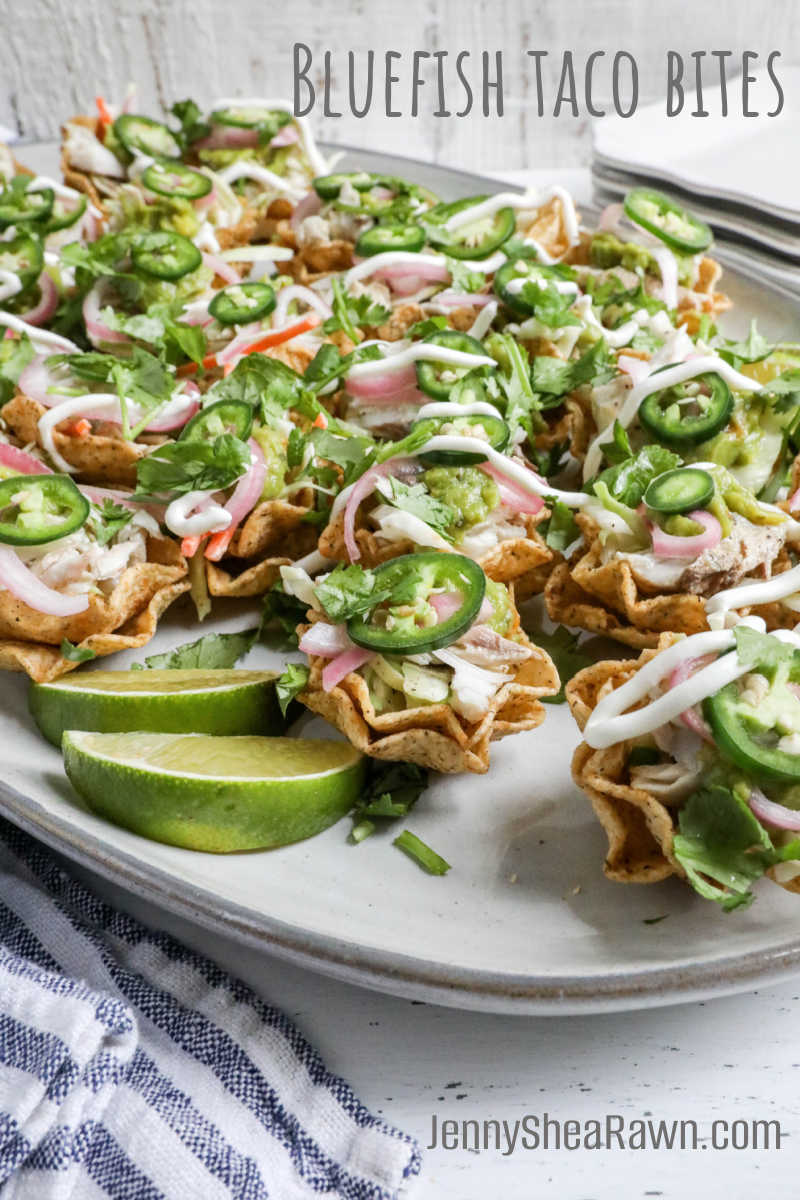 An image for a bluefish taco bite recipe on a white platter with lime wedges.