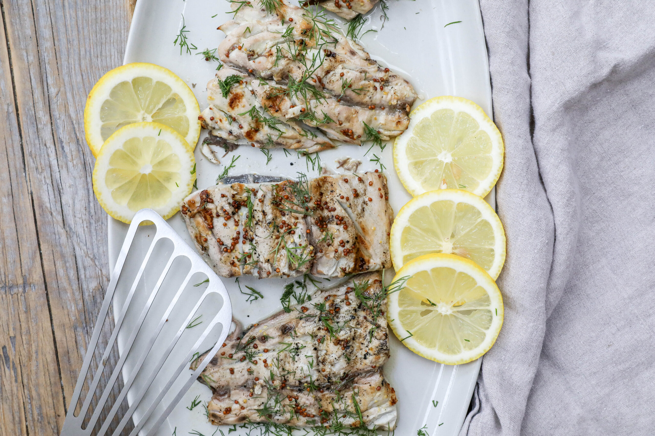 An image of bluefish fillets with lemon slices and dill on a white plate.