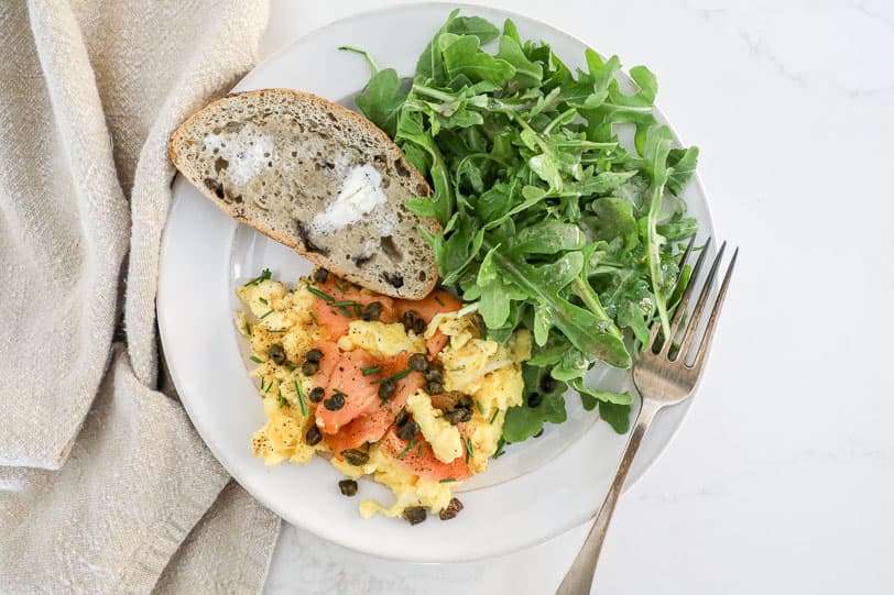 An overhead image of smoked salmon eggs with toast and an arugula salad. 