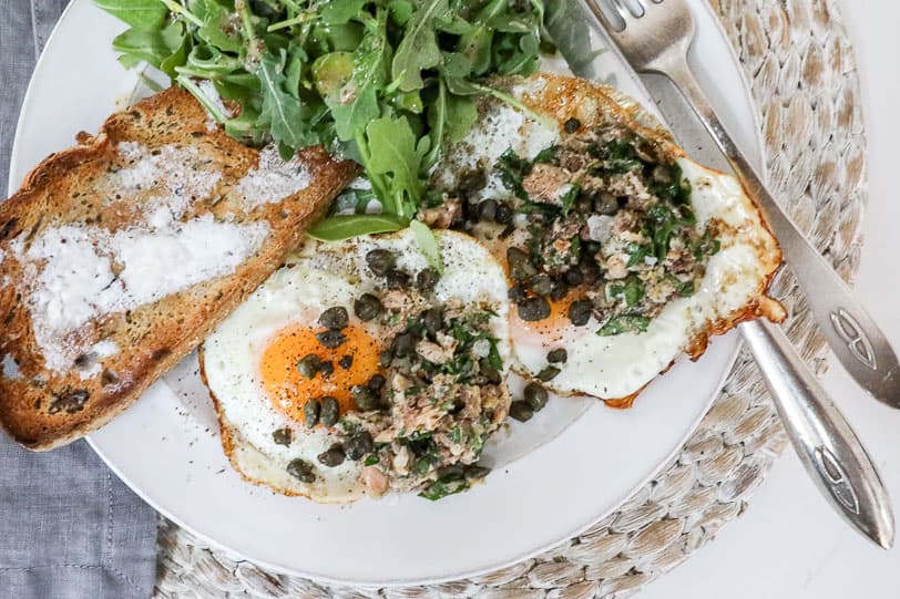 An overhead image of sardines with eggs on a white plate.