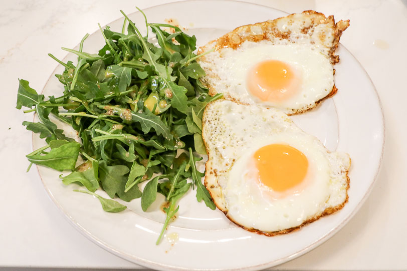 An image of fried eggs with arugula on the side. 