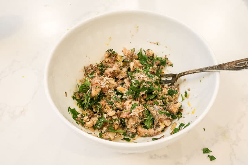 An image of sardines in a white bowl with lemon zest and parsley. 