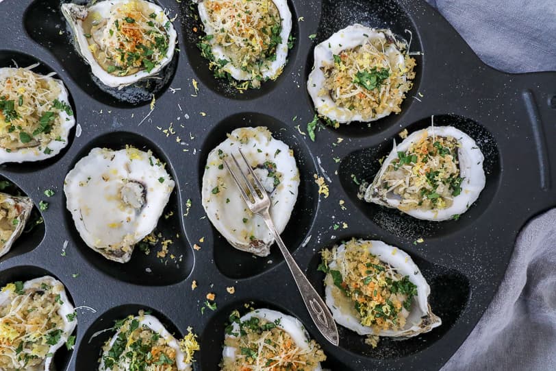 An overhead image of roasted oysters in a cast iron oyster pan. 