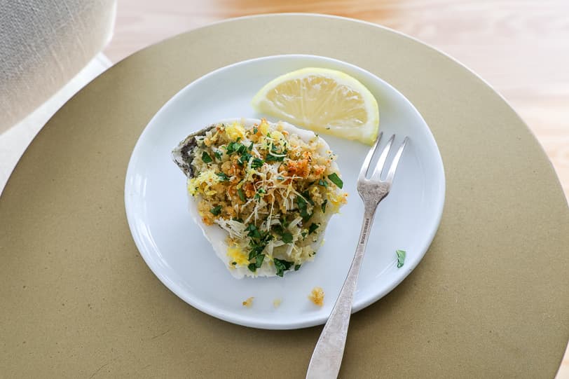 A roasted oyster with breadcrumbs on a white plate. 