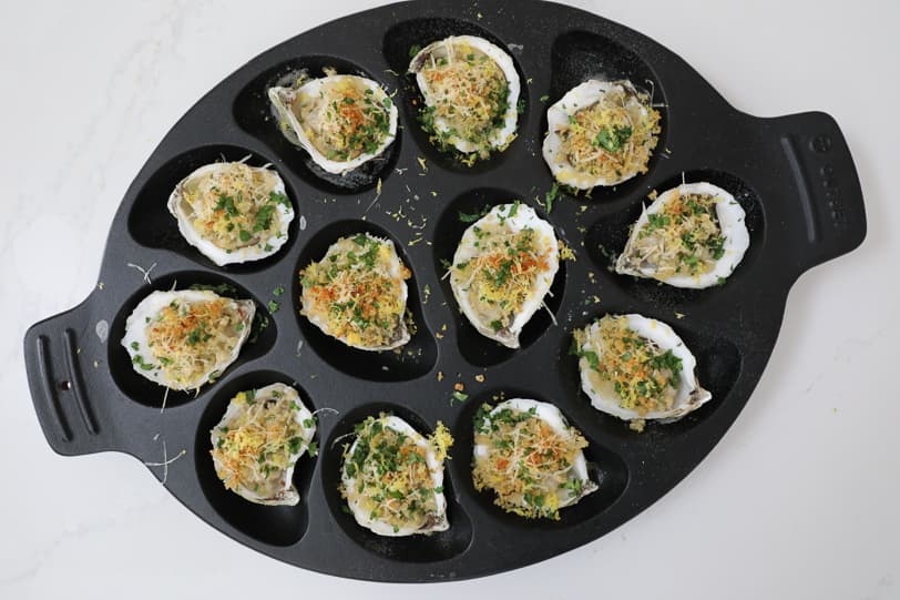 Roasted oysters in a cast-iron oyster pan on a white countertop. 