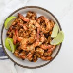 An image of cumin shrimp in a white bowl with limes.