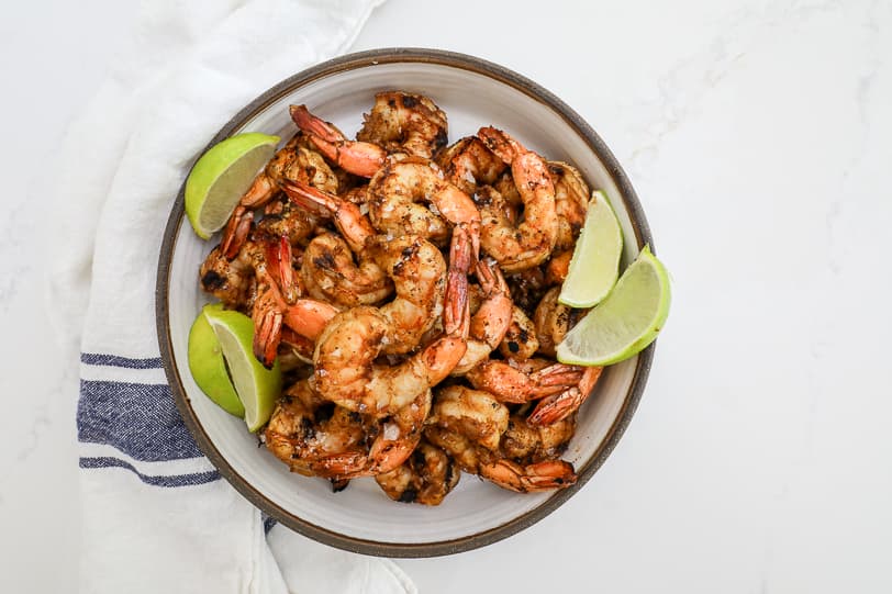 An image of cumin shrimp in a white bowl with limes.