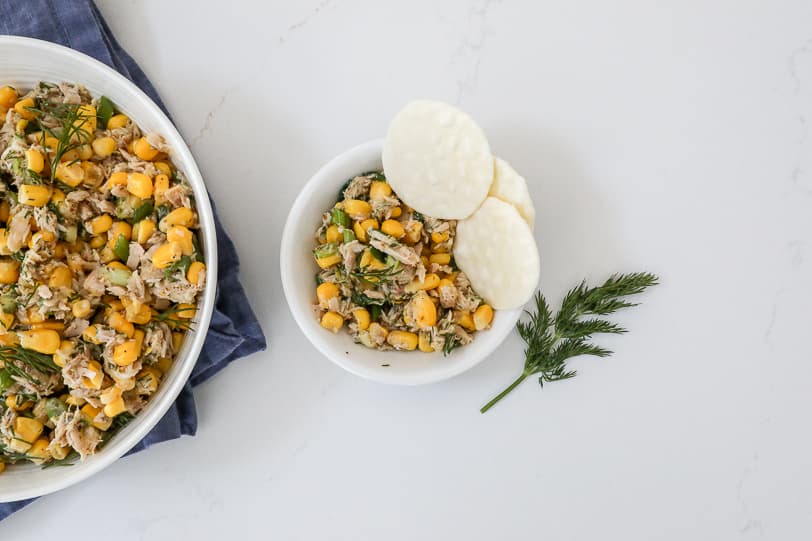 An image of corn and tuna salad in a small bowl with rice crackers.