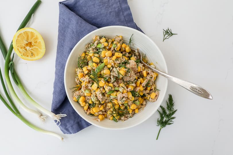 An image of tuna corn salad in a white bowl with scallions and dill scattered around.